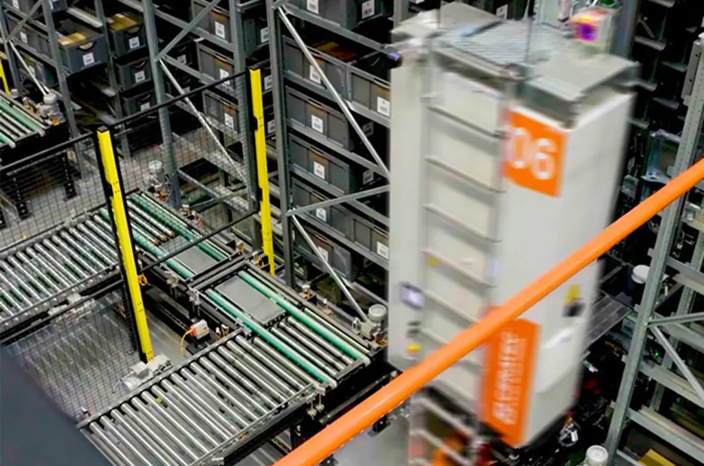 Almacén automatizado con cintas transportadoras y un robot de almacenamiento de alta velocidad que se desplaza entre estanterías altas con contenedores.