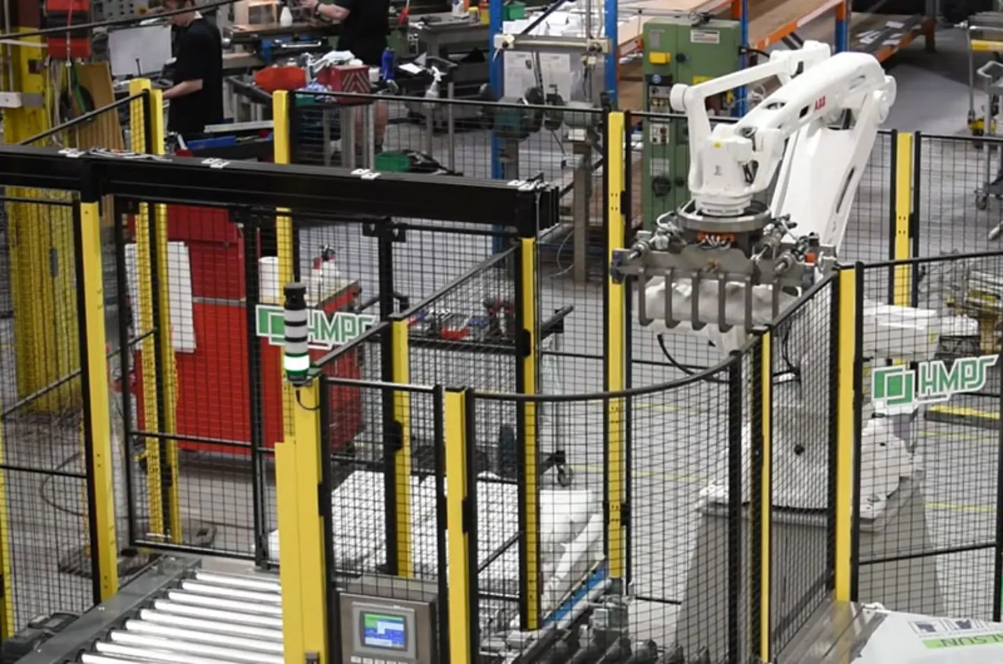 Brazo robótico industrial automatizado operando en una fábrica con sistemas de transporte y vallado de seguridad.
