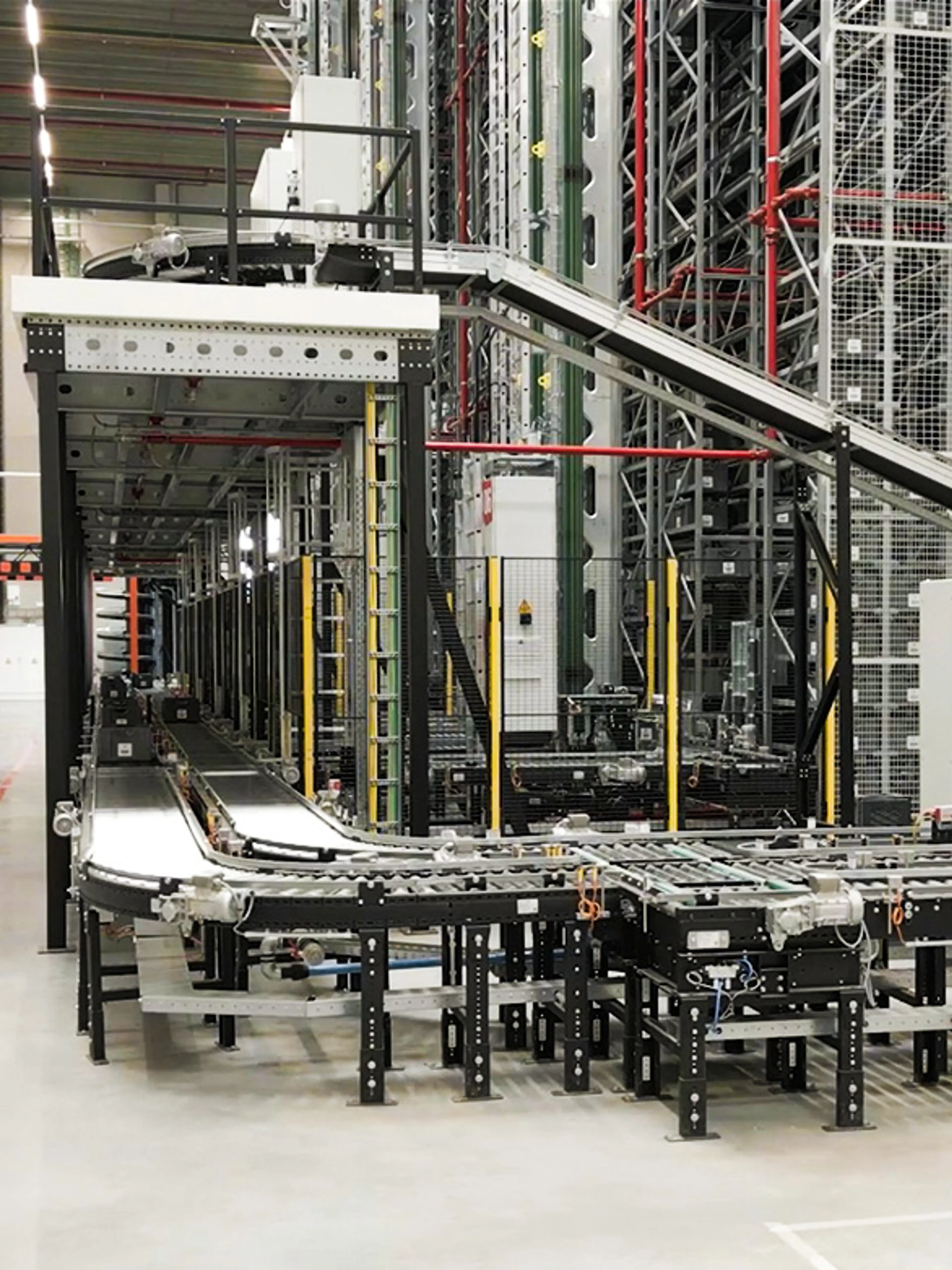 Sistema automatizado de transportadores de rodillos y banda en un almacén, utilizado para el transporte de contenedores y cajas.