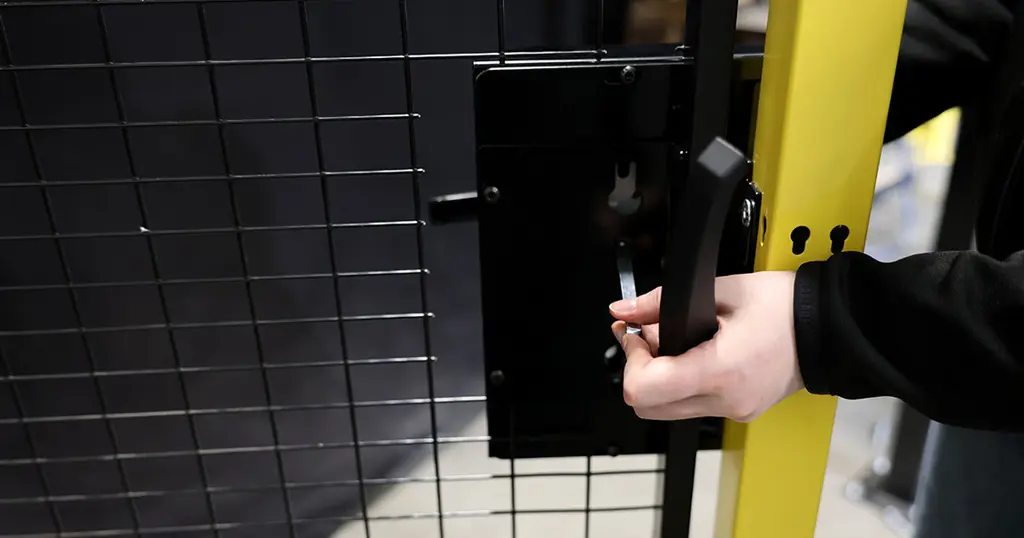 Mano sujetando una cerradura de bombillo montada sobre un panel de malla negra