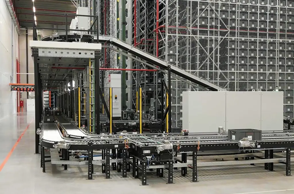 Sistema automatizado de transporte por rodillos y cintas en un almacén, utilizado para trasladar contenedores y cajas (totes y bins).